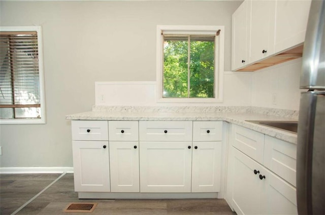 kitchen featuring visible vents, baseboards, freestanding refrigerator, wood finished floors, and white cabinets