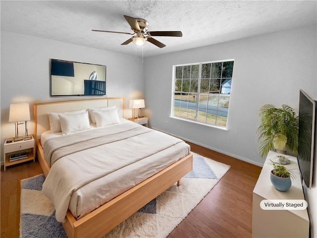 bedroom with a ceiling fan, a textured ceiling, baseboards, and wood finished floors