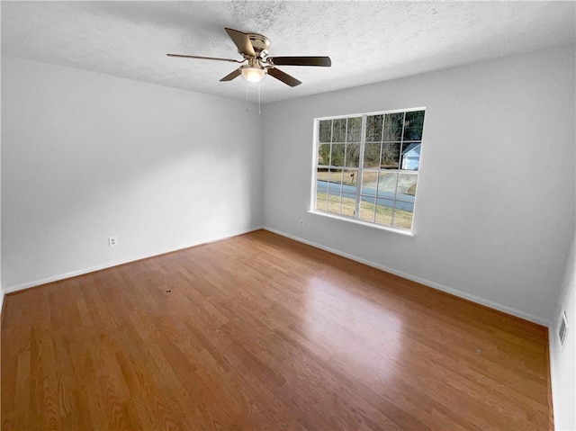 unfurnished room with ceiling fan, a textured ceiling, baseboards, and wood finished floors