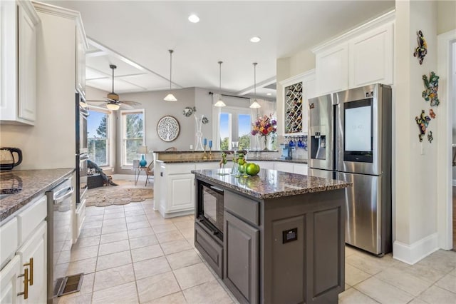 kitchen featuring stainless steel appliances, a kitchen island, white cabinetry, pendant lighting, and dark stone countertops