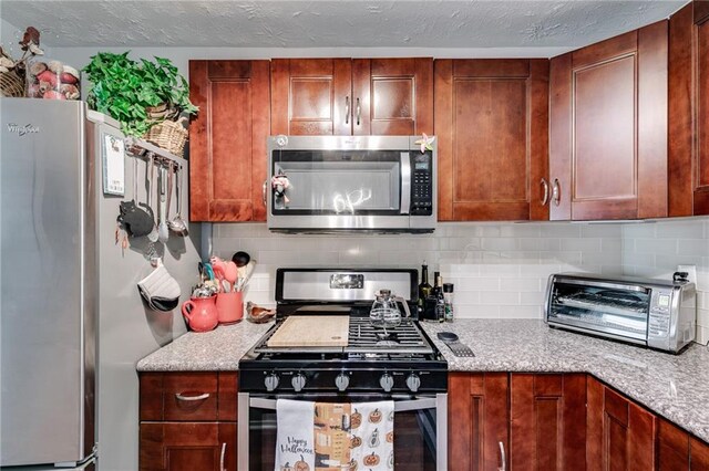 kitchen featuring backsplash, stainless steel appliances, light stone countertops, and a toaster