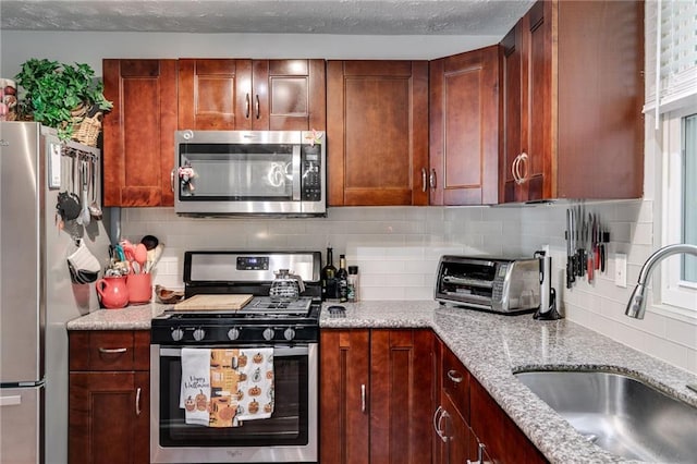 kitchen featuring light stone counters, appliances with stainless steel finishes, a sink, a toaster, and tasteful backsplash