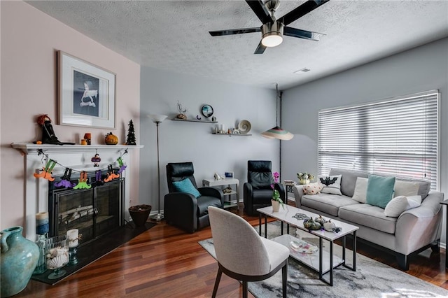 living area with a ceiling fan, a textured ceiling, and wood finished floors