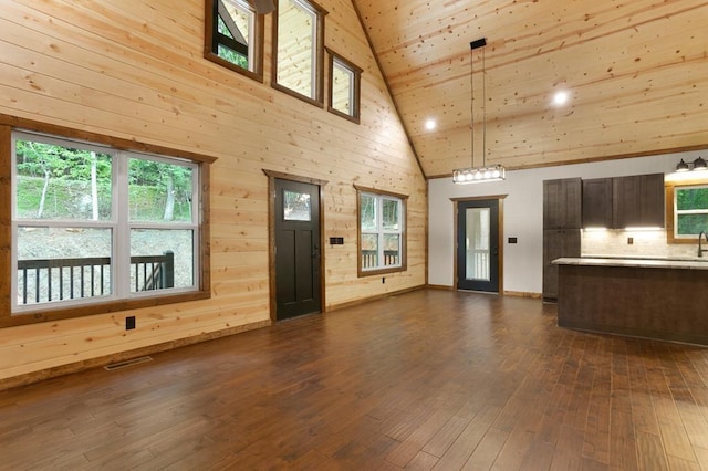 unfurnished living room featuring a wealth of natural light, wood walls, dark hardwood / wood-style flooring, and high vaulted ceiling