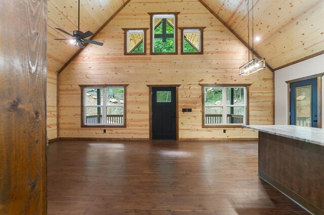 unfurnished living room with high vaulted ceiling, wood walls, and dark hardwood / wood-style flooring