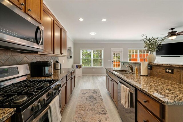 kitchen with crown molding, a sink, light wood-style flooring, stainless steel appliances, and tasteful backsplash