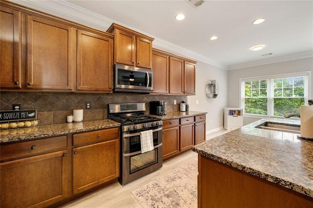kitchen with dark stone counters, appliances with stainless steel finishes, ornamental molding, and brown cabinetry