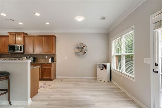 kitchen with brown cabinets, stainless steel microwave, visible vents, and ornamental molding