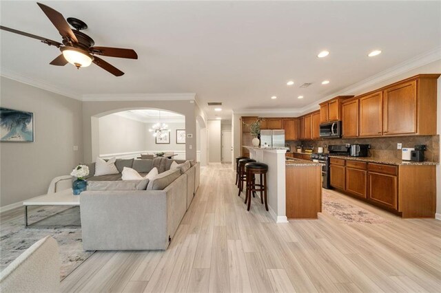 living area with crown molding, light wood-style floors, arched walkways, ceiling fan with notable chandelier, and recessed lighting