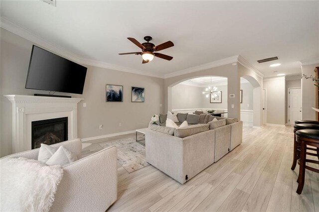 living area featuring crown molding, arched walkways, and light wood-style floors
