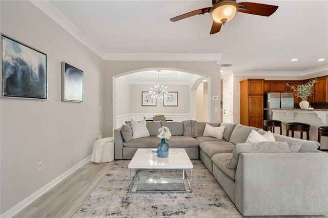 living room featuring ornamental molding, baseboards, arched walkways, light wood finished floors, and ceiling fan with notable chandelier