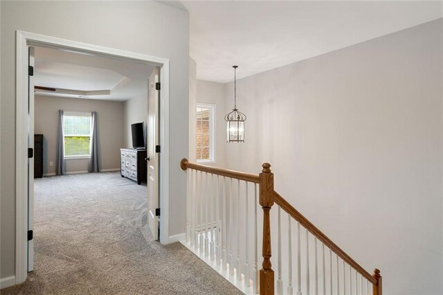 corridor with carpet floors, baseboards, a notable chandelier, and an upstairs landing