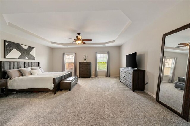 bedroom with a ceiling fan, a tray ceiling, light colored carpet, and multiple windows