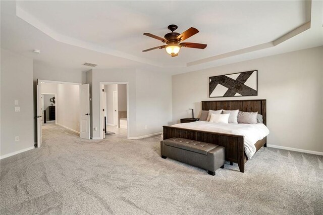 carpeted bedroom featuring ceiling fan, visible vents, baseboards, connected bathroom, and a tray ceiling