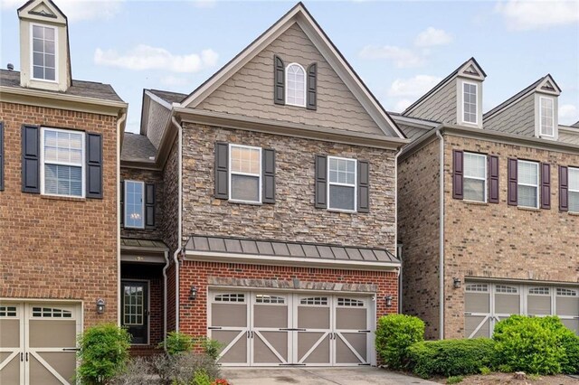 view of property featuring an attached garage, driveway, brick siding, and a standing seam roof