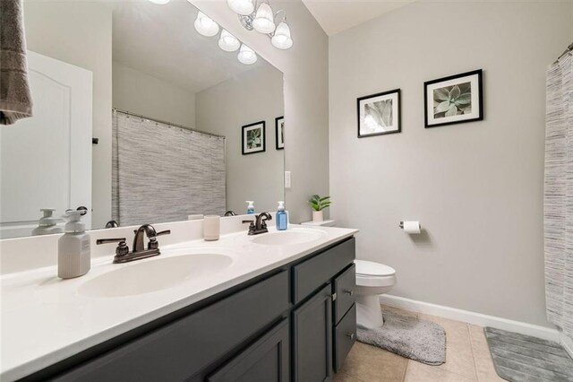 bathroom with double vanity, a sink, tile patterned floors, and toilet