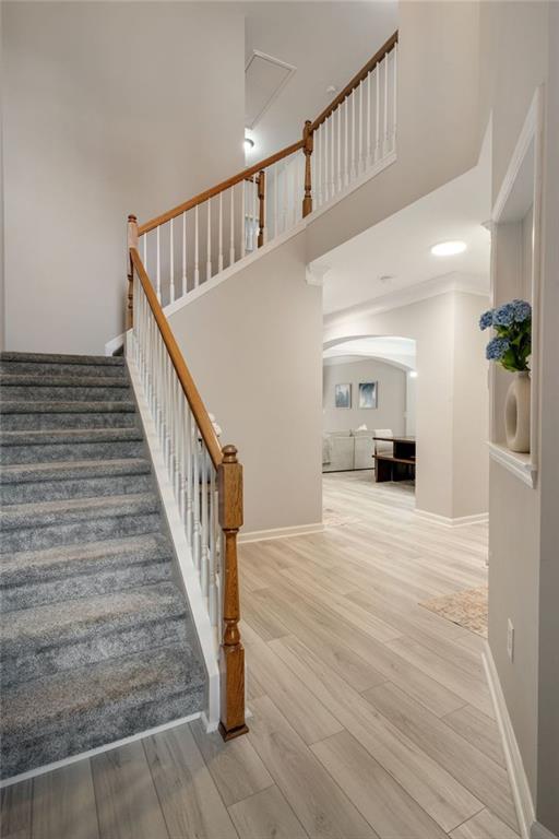 staircase featuring baseboards, a high ceiling, arched walkways, and wood finished floors
