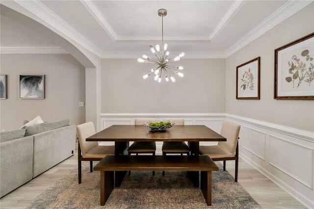dining area with crown molding, a raised ceiling, a chandelier, arched walkways, and light wood finished floors