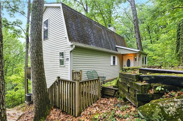 rear view of house with a gambrel roof, roof with shingles, and a chimney