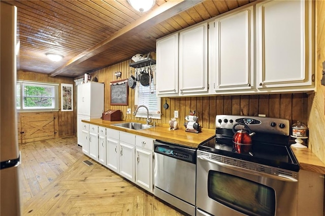 kitchen featuring wood walls, a sink, wooden ceiling, white cabinets, and stainless steel appliances