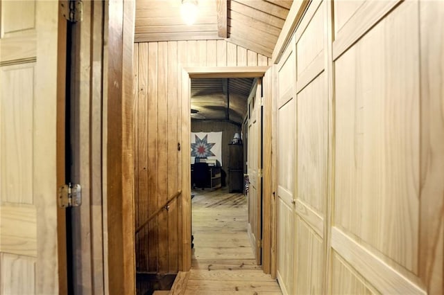 hallway with wood ceiling, light wood finished floors, vaulted ceiling, and wood walls