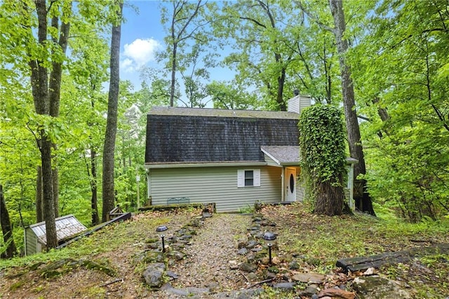 back of house with roof with shingles and a chimney