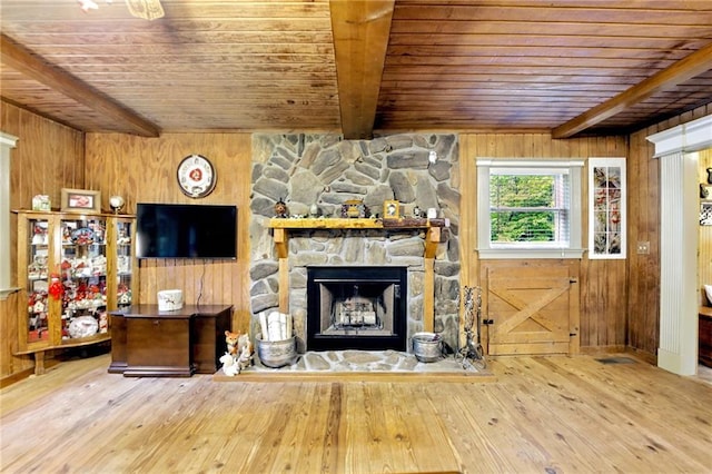 living room featuring wood-type flooring, wood walls, a stone fireplace, beamed ceiling, and wood ceiling