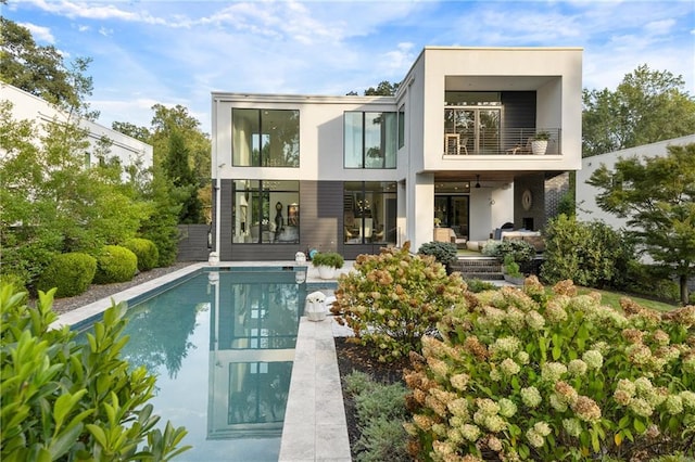 back of property featuring an outdoor pool, a balcony, and stucco siding