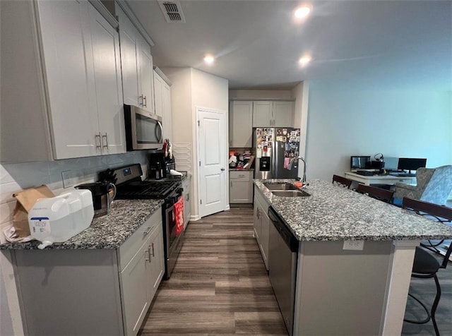 kitchen with a kitchen island with sink, backsplash, a kitchen breakfast bar, and stainless steel appliances