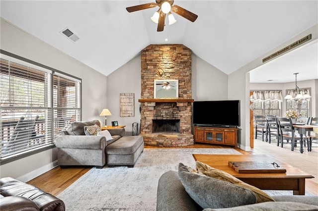 living room with ceiling fan, a chandelier, baseboards, a stone fireplace, and high vaulted ceiling
