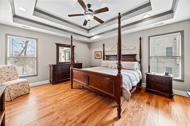 bedroom featuring a tray ceiling, crown molding, baseboards, recessed lighting, and light wood finished floors