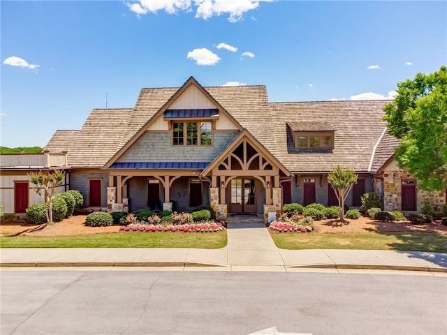 view of front of house featuring stone siding, covered porch, and a standing seam roof