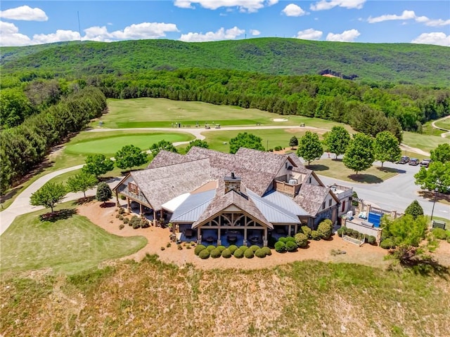 aerial view of property and surrounding area with a heavily wooded area, a golf club, and a mountainous background