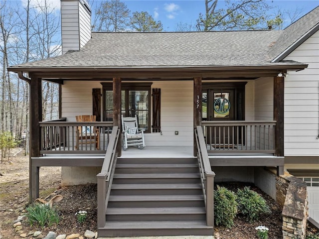 view of exterior entry with roof with shingles, a chimney, and covered porch