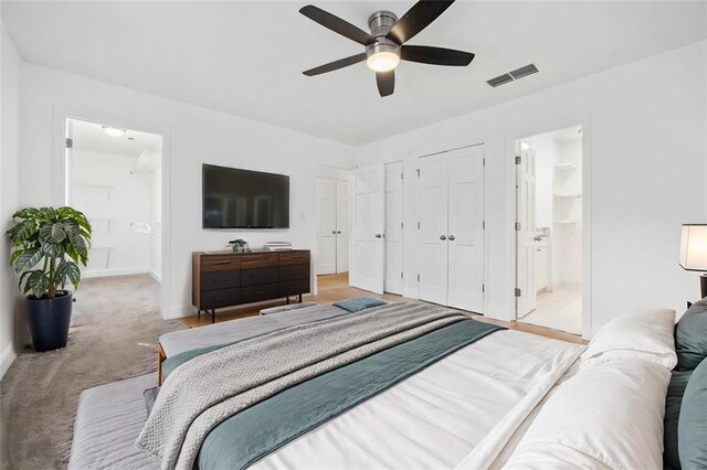 carpeted bedroom featuring multiple closets, ceiling fan, and ensuite bath