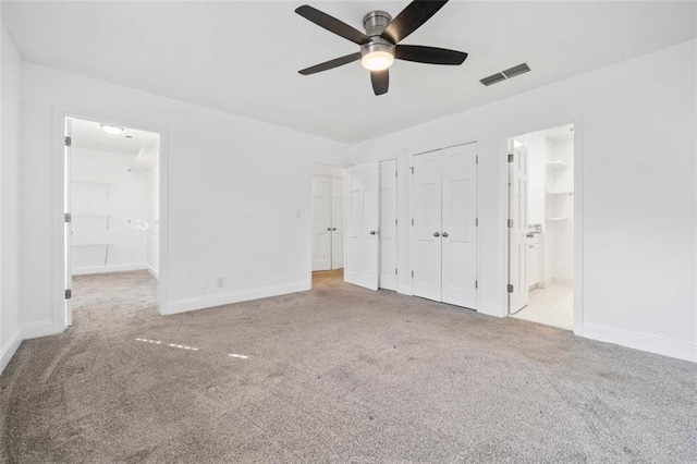 unfurnished bedroom featuring ceiling fan, light colored carpet, ensuite bathroom, and two closets