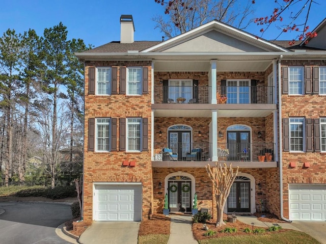 view of front facade featuring a balcony, brick siding, driveway, french doors, and a chimney