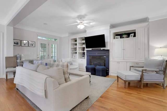 living room featuring crown molding, a glass covered fireplace, built in features, and light wood-style floors