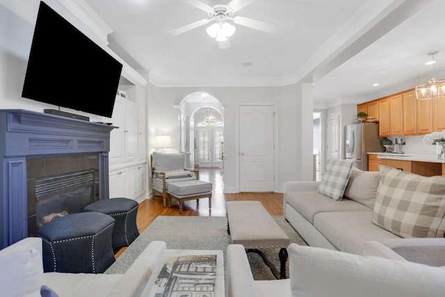 living area with arched walkways, french doors, ornamental molding, light wood finished floors, and a glass covered fireplace