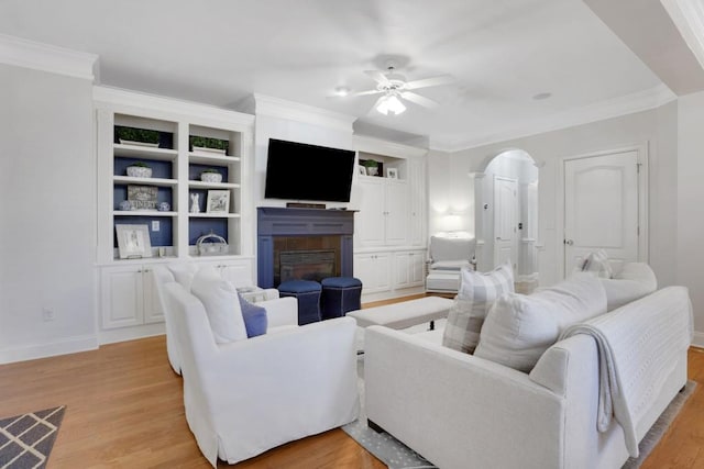 living area featuring arched walkways, light wood finished floors, a glass covered fireplace, and crown molding