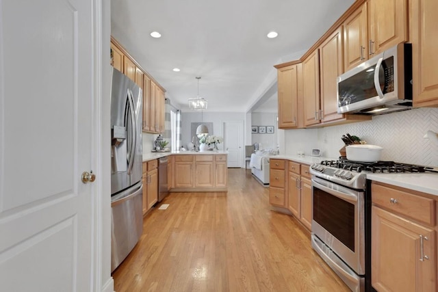 kitchen with light wood finished floors, decorative backsplash, appliances with stainless steel finishes, a peninsula, and light countertops