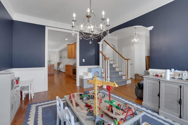 dining area featuring arched walkways, a wainscoted wall, wood finished floors, stairway, and an inviting chandelier