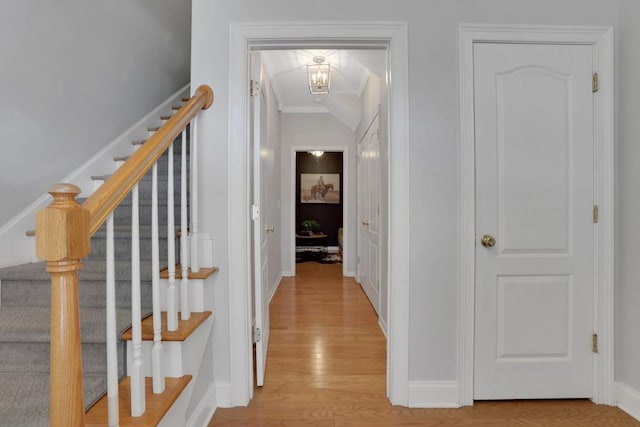 hallway with ornamental molding, light wood-type flooring, stairway, and baseboards