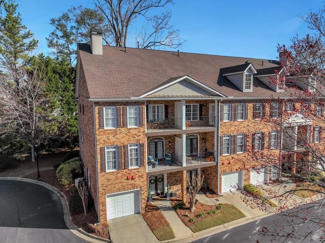 view of front facade featuring an attached garage, a balcony, brick siding, concrete driveway, and a chimney