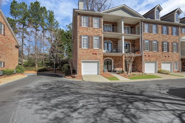 multi unit property with driveway, brick siding, a chimney, and an attached garage