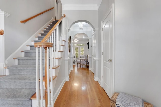 interior space with arched walkways, crown molding, light wood finished floors, and stairs