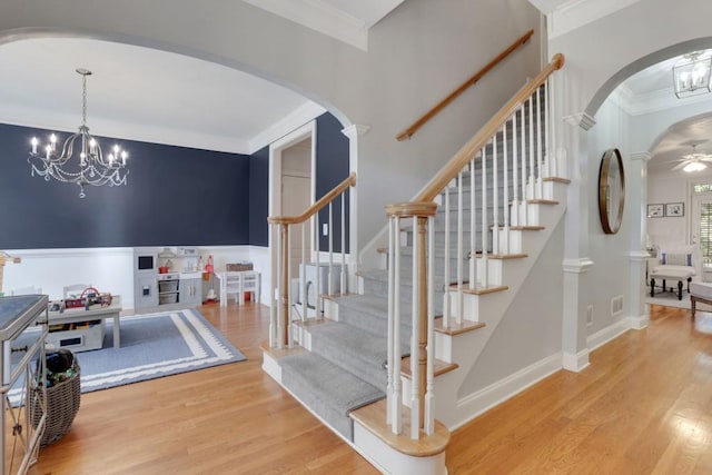 stairs featuring ornamental molding, arched walkways, ceiling fan with notable chandelier, and wood finished floors