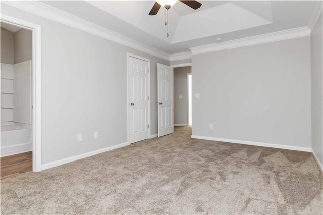 unfurnished bedroom with connected bathroom, carpet flooring, ornamental molding, ceiling fan, and a tray ceiling