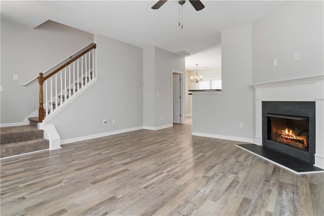 unfurnished living room with ceiling fan with notable chandelier and light wood-type flooring