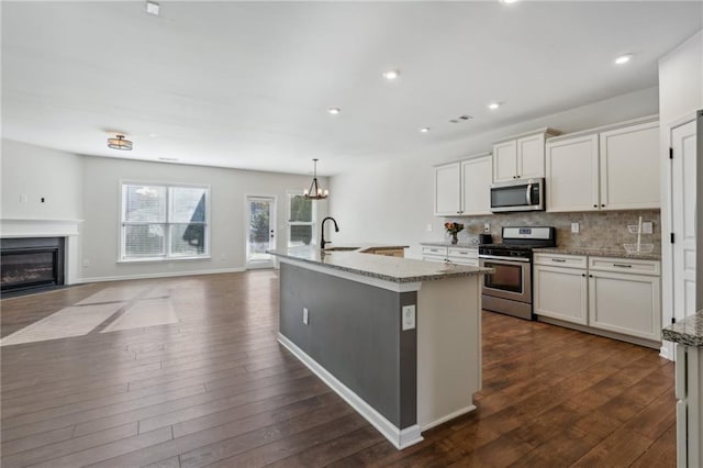 kitchen featuring backsplash, white cabinets, a kitchen island with sink, dark wood-type flooring, and appliances with stainless steel finishes